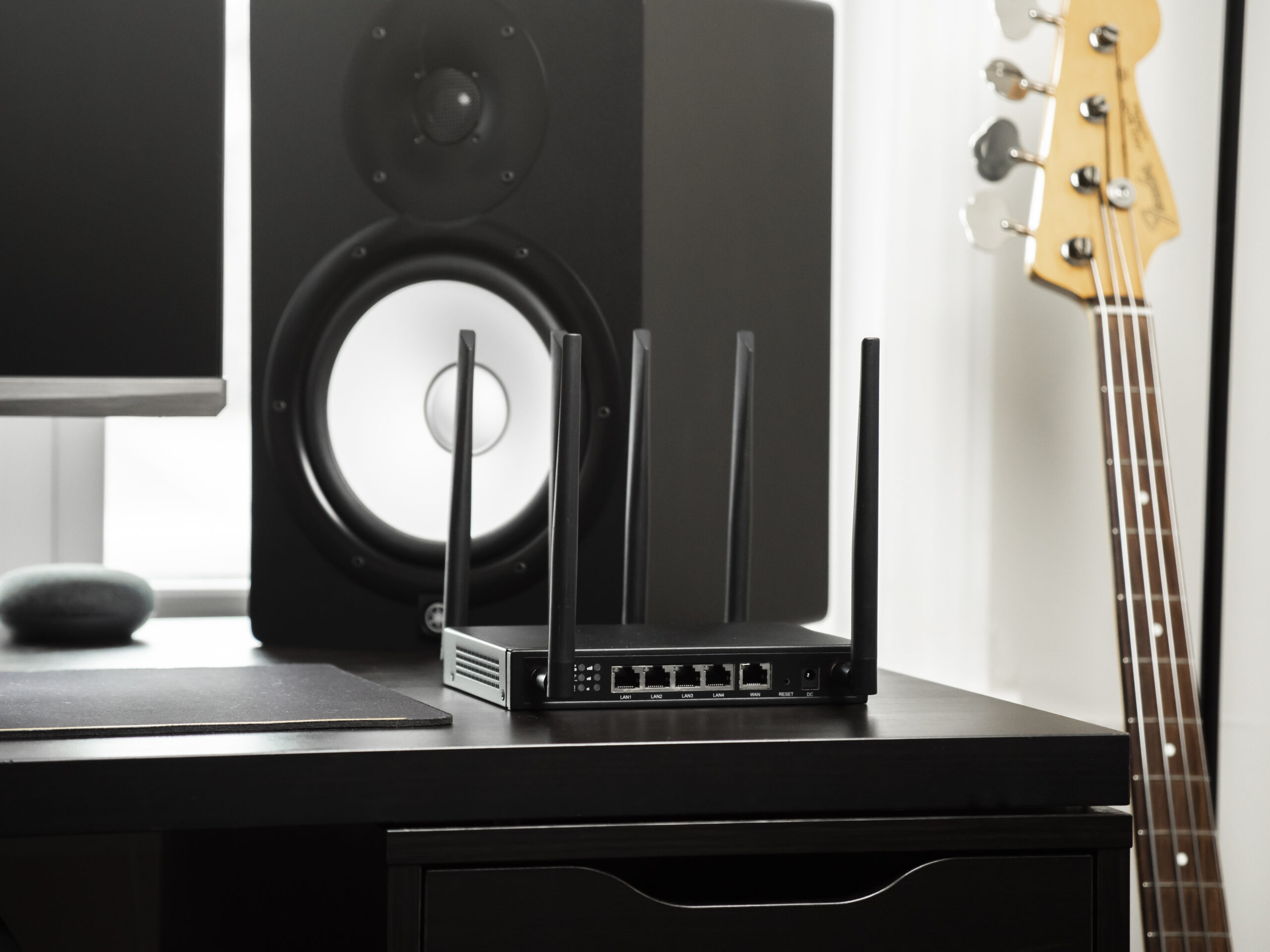 X-LINK router on black furniture next to a studio monitor speaker with bass guitar neck visible.