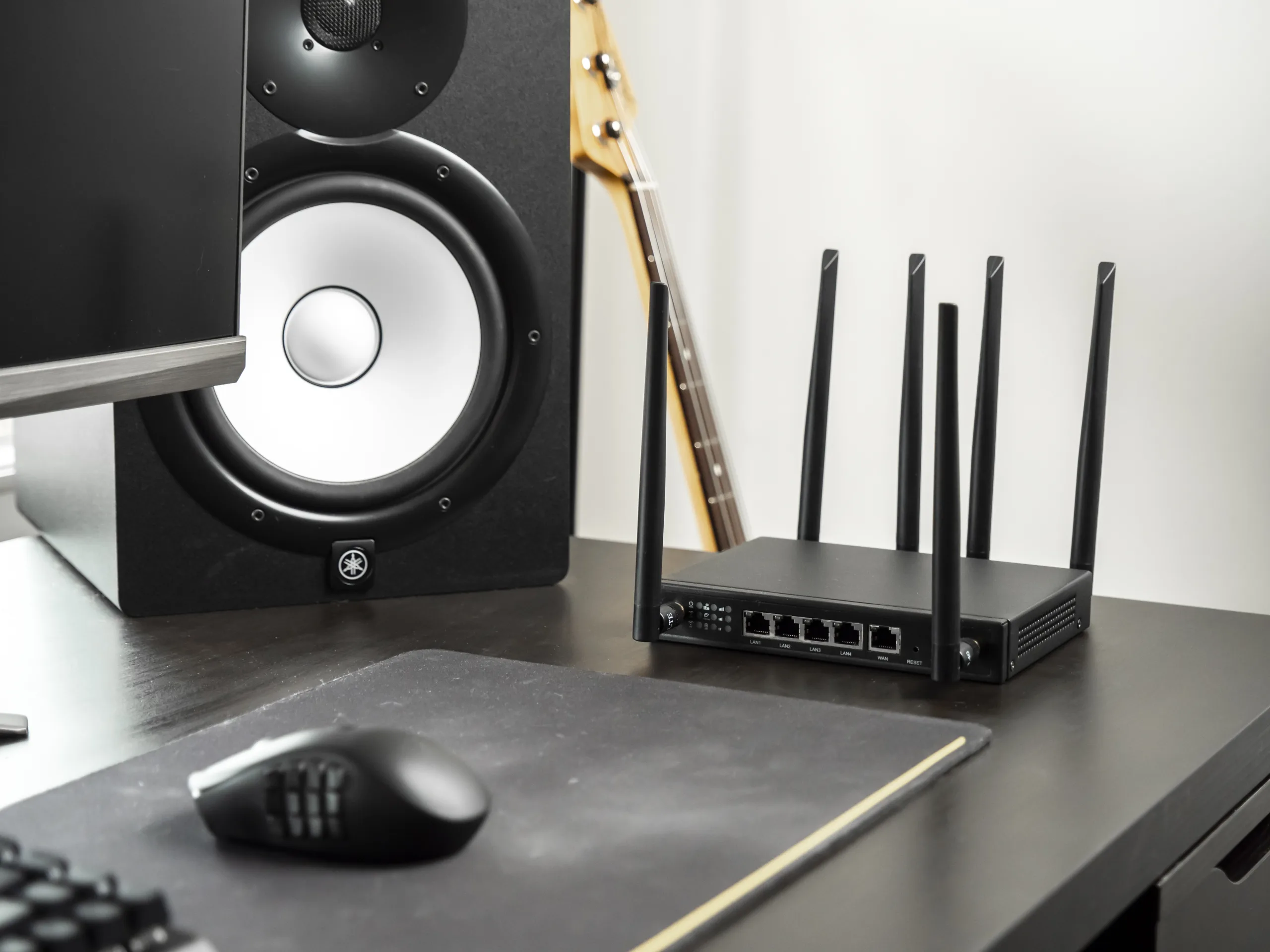 X-LINK router on a dark desk surface with Yamaha studio speaker, computer mouse, and bass guitar neck in frame.