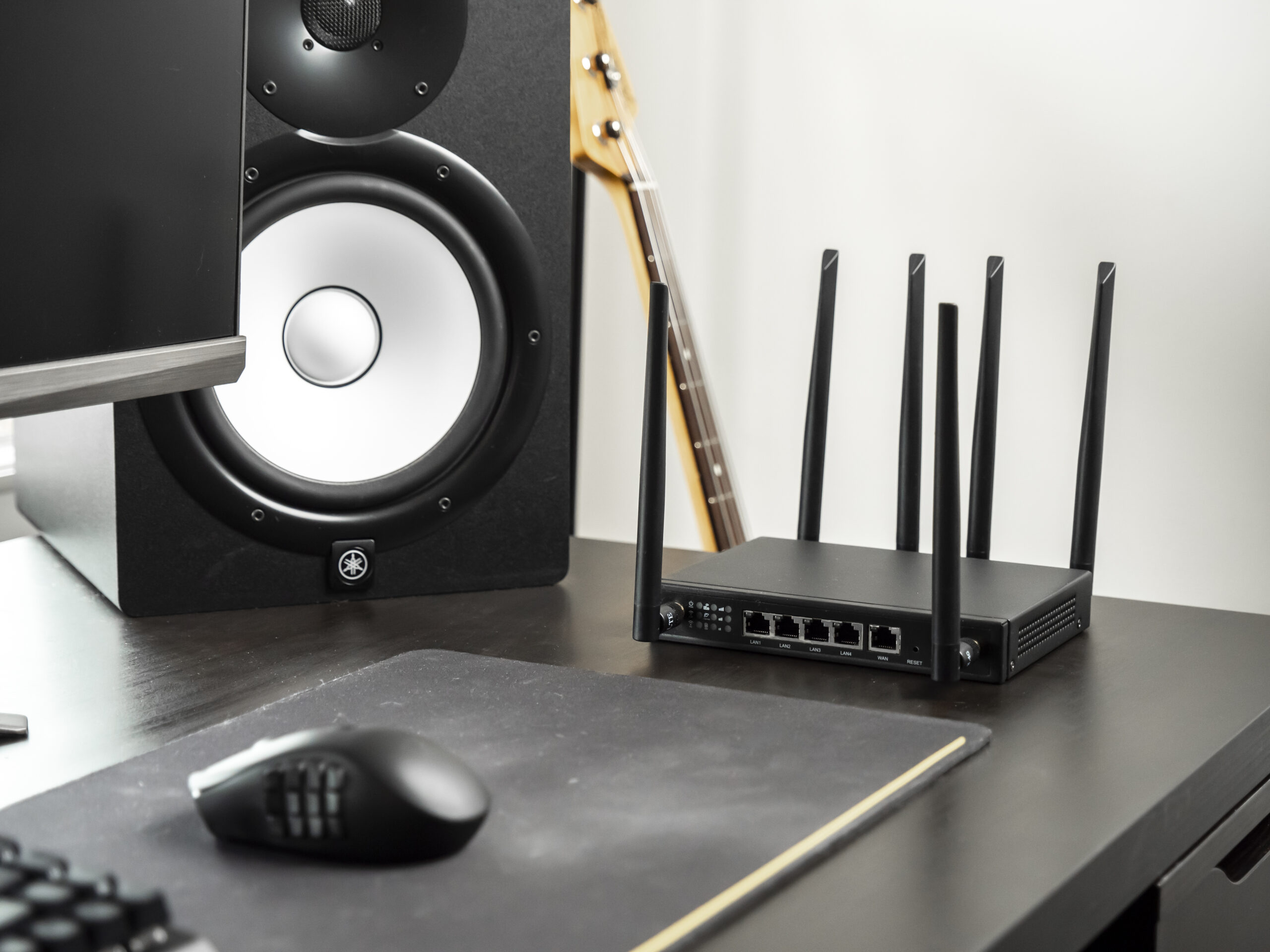 X-LINK router on a dark desk surface with Yamaha studio speaker, computer mouse, and bass guitar neck in frame.