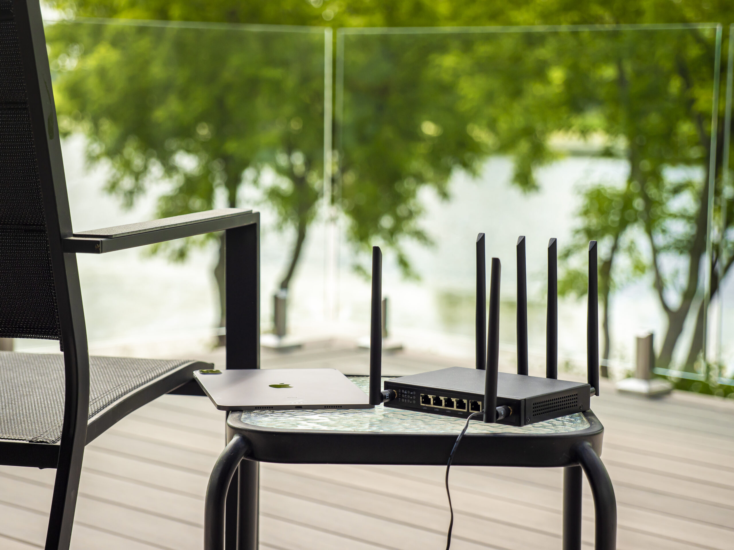 X-LINK router and white laptop positioned on a round stool near large windows with green foliage visible outside.